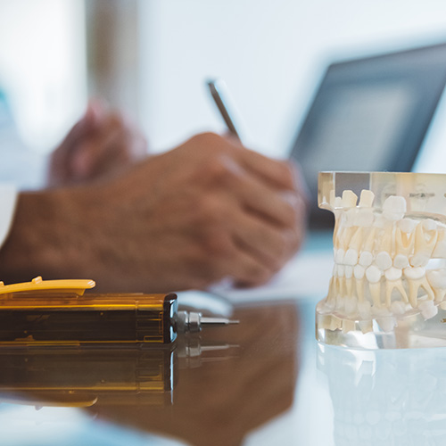 Close-up of a dentist’s hand writing while they reference a DataDx report on their computer