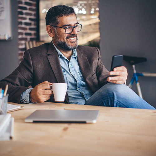 a practice owner checking their phone with a cup of coffee, their laptop sitting closed on the desk